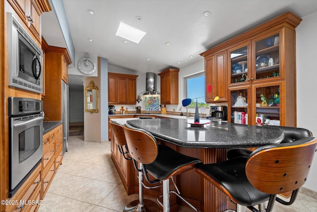 6731 N Pontatoc Rd, Tucson, AZ 85718 - kitchen featuring appliances with stainless steel finishes, a skylight, vaulted ceiling, wall chimney range hood, and a breakfast bar area