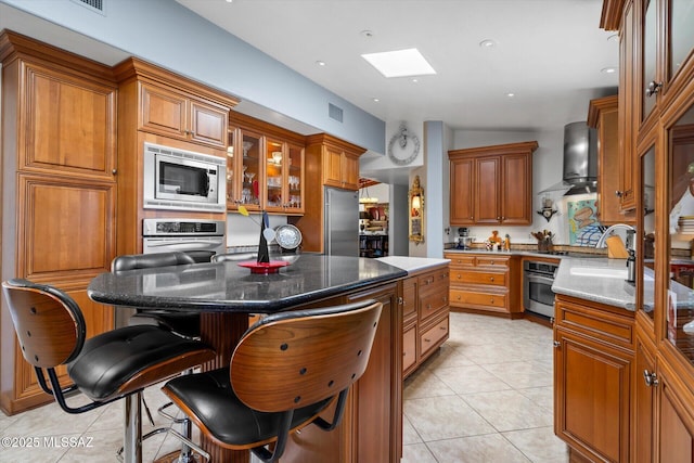 6731 N Pontatoc Rd, Tucson, AZ 85718 - kitchen with wall chimney exhaust hood, appliances with stainless steel finishes, brown cabinetry, a skylight, and a sink