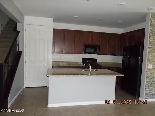 902 W Calle Tipoy, Sahuarita, AZ 85629 - kitchen with black appliances, light stone countertops, a kitchen island with sink, dark tile patterned flooring, and baseboards