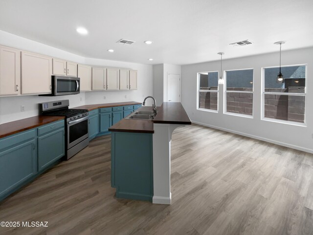 7637 E Cholla Overlook Dr, Tucson, AZ 85710 - kitchen featuring stainless steel appliances, a sink, wood finished floors, blue cabinets, and hanging light fixtures