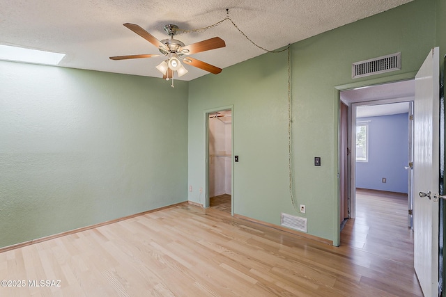 7821 N Jensen Dr, Tucson, AZ 85741 - unfurnished bedroom featuring wood finished floors, a closet, a walk in closet, a textured ceiling, and a skylight