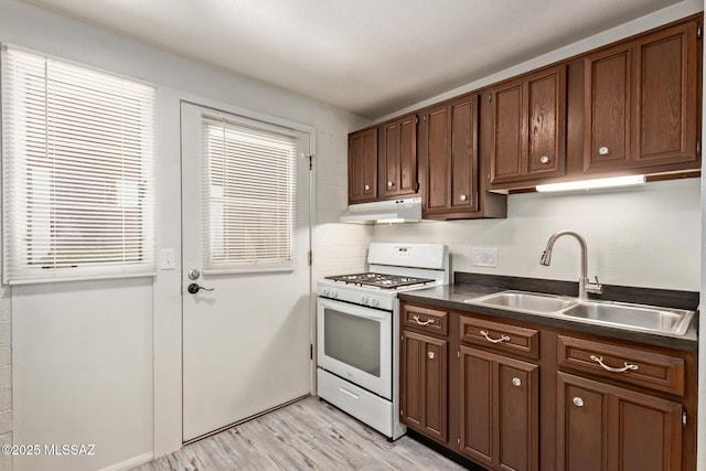 134 S Paseo Quinta Unit A, Green Valley, AZ 85614 - kitchen with white gas range, a sink, dark countertops, under cabinet range hood, and light wood-style floors