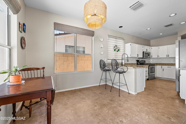 9860 N Western Sky Pl, Tucson, AZ 85742 - kitchen with stainless steel appliances, a peninsula, white cabinets, a chandelier, and baseboards