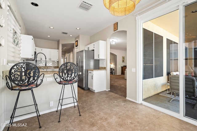 9860 N Western Sky Pl, Tucson, AZ 85742 - kitchen with arched walkways, a peninsula, freestanding refrigerator, a kitchen bar, and white cabinets