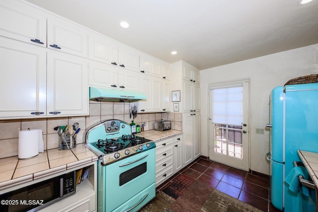 2600 E Skyline Dr Unit 21, Tucson, AZ 85718 - kitchen featuring range with gas cooktop, under cabinet range hood, white cabinetry, stainless steel microwave, and tasteful backsplash
