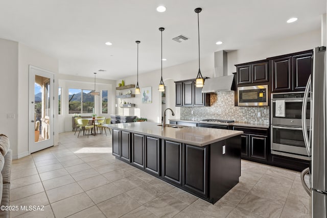 12475 N Faraway Wash Trl, Marana, AZ 85658 - kitchen featuring appliances with stainless steel finishes, wall chimney range hood, tasteful backsplash, light countertops, and a center island with sink