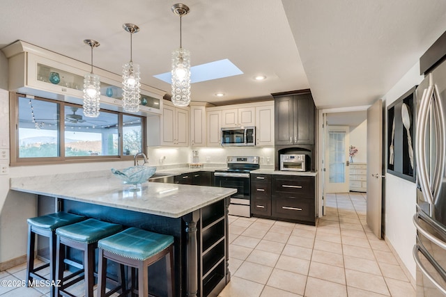 4990 N Kolb Rd, Tucson, AZ 85750 - kitchen featuring appliances with stainless steel finishes, a skylight, a peninsula, light tile patterned flooring, and light stone countertops