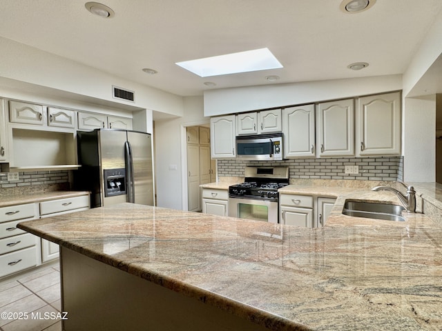 7621 N Placita De Los Amigos, Tucson, AZ 85704 - kitchen featuring appliances with stainless steel finishes, a skylight, tasteful backsplash, a peninsula, and light tile patterned floors