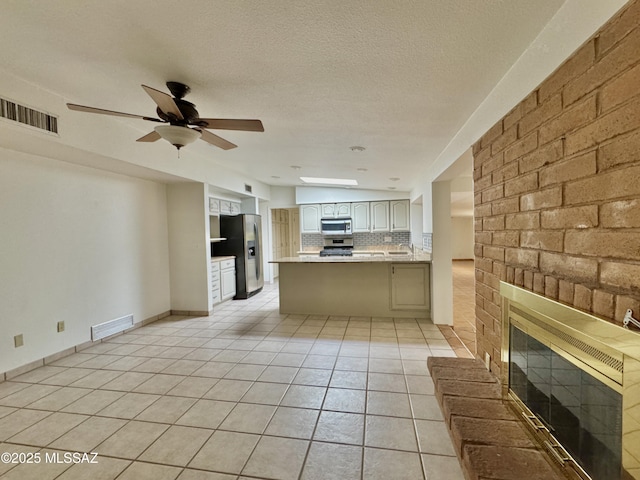 7621 N Placita De Los Amigos, Tucson, AZ 85704 - kitchen featuring stainless steel appliances, a peninsula, light tile patterned floors, a brick fireplace, and tasteful backsplash