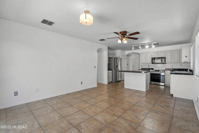 9969 E Apache Rain Dr, Tucson, AZ 85748 - kitchen featuring stainless steel appliances, dark countertops, arched walkways, a ceiling fan, and a kitchen island