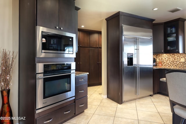 8142 N Modena Dr, Tucson, AZ 85742 - kitchen featuring built in appliances, light tile patterned floors, decorative backsplash, dark brown cabinetry, and glass insert cabinets