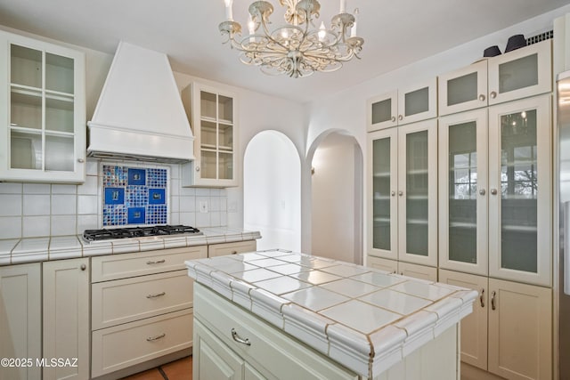 5015 N Via Condesa, Tucson, AZ 85718 - kitchen with custom exhaust hood, stainless steel gas stovetop, tile counters, a chandelier, and backsplash