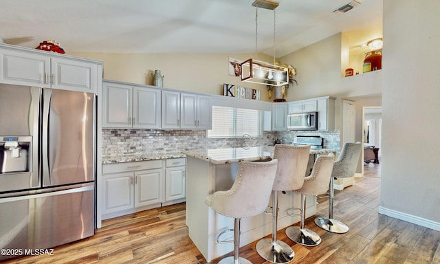8942 N Ferber Ct, Tucson, AZ 85742 - kitchen featuring appliances with stainless steel finishes, backsplash, light wood-style flooring, light stone countertops, and a kitchen breakfast bar