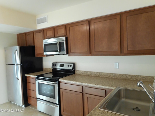 1809 E Miles St, Tucson, AZ 85719 - kitchen with appliances with stainless steel finishes, brown cabinetry, light countertops, and light tile patterned floors