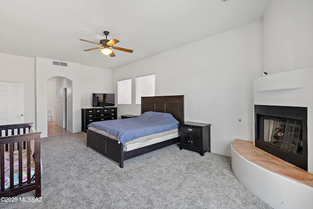 11120 E Mountain Gate Pl, Tucson, AZ 85749 - bedroom featuring arched walkways, light carpet, a fireplace with raised hearth, and a ceiling fan
