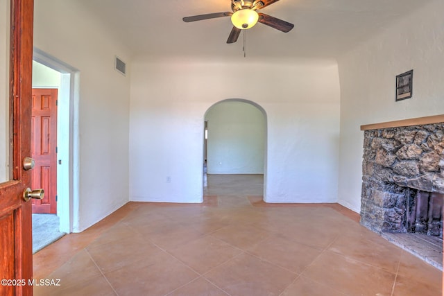 1125 W Huron St, Tucson, AZ 85745 - unfurnished living room with arched walkways, a stone fireplace, ceiling fan, and tile patterned floors