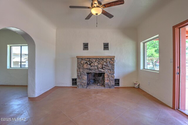 1125 W Huron St, Tucson, AZ 85745 - unfurnished living room featuring a ceiling fan, tile patterned floors, a stone fireplace, and arched walkways