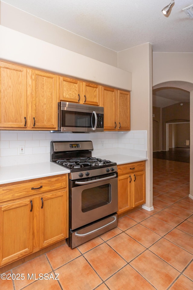5566 W Dove Of Peace Dr, Marana, AZ 85658 - kitchen featuring stainless steel appliances, arched walkways, light tile patterned floors, light countertops, and tasteful backsplash
