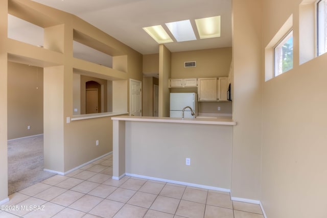 13491 N Tom Ryans Way, Oro Valley, AZ 85755 - kitchen with freestanding refrigerator, a peninsula, light countertops, a skylight, and vaulted ceiling