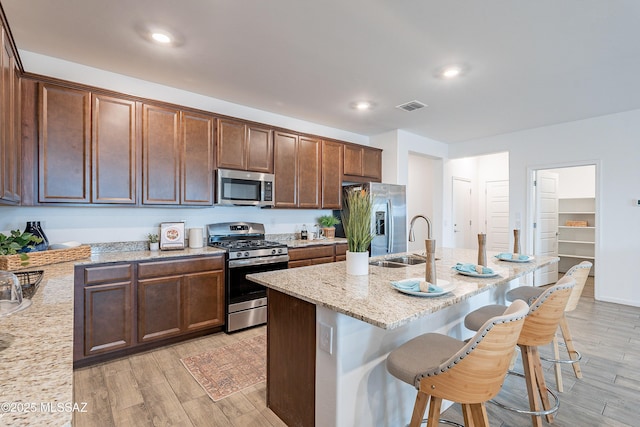 10490 W Beaman Ln, Marana, AZ 85653 - kitchen featuring stainless steel appliances, light wood-style flooring, a breakfast bar area, light stone countertops, and an island with sink