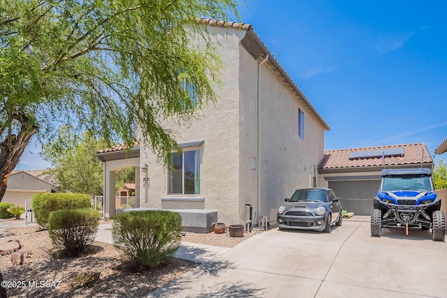 10567 E Desert Drifter Pl, Tucson, AZ 85747 - view of side of property featuring stucco siding, driveway, roof mounted solar panels, an attached garage, and a tiled roof