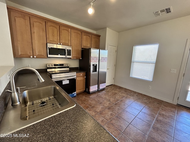 3365 N River Rapids Dr, Tucson, AZ 85712 - kitchen with stainless steel appliances, dark countertops, brown cabinetry, track lighting, and dark tile patterned flooring