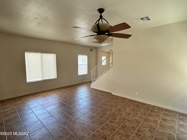 3365 N River Rapids Dr, Tucson, AZ 85712 - unfurnished room with a ceiling fan, stairway, dark tile patterned floors, and a textured ceiling
