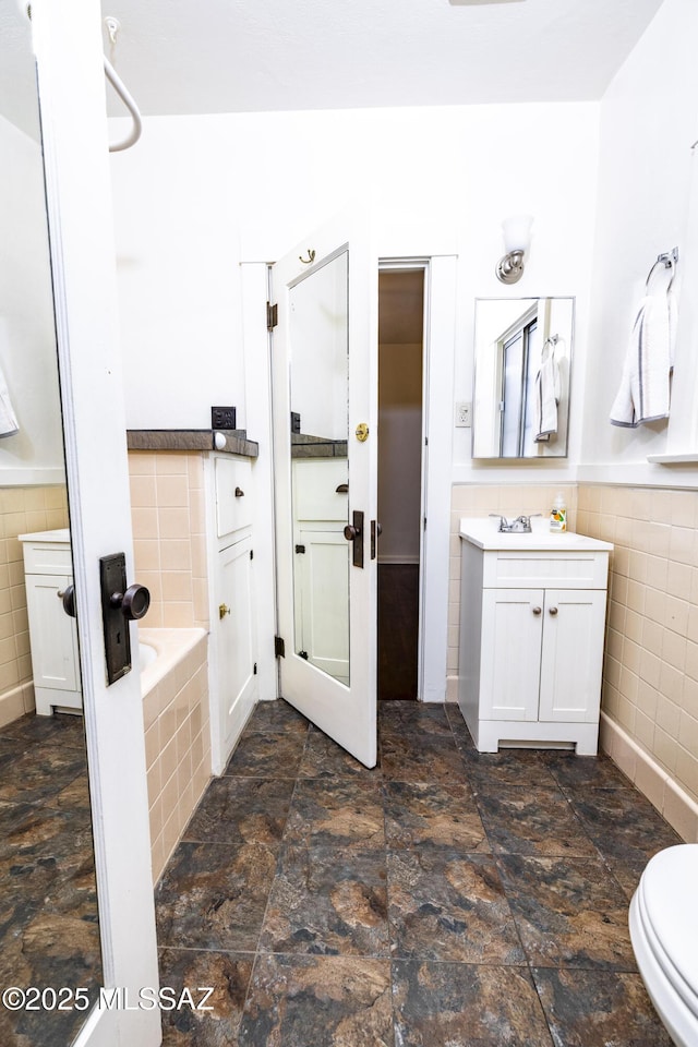 1809 E 8th St, Tucson, AZ 85719 - bathroom with tile walls, a bath, vanity, stone finish floors, and a wainscoted wall