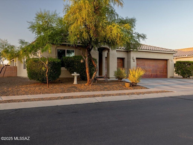 3872 W Sonoma Ranch Pl, Marana, AZ 85658 - view of property hidden behind natural elements featuring an attached garage, concrete driveway, stucco siding, and a tile roof