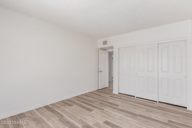64161 E Santa Catalina Ct, Saddlebrooke, AZ 85739 - unfurnished bedroom with light wood-type flooring, a textured ceiling, and a closet