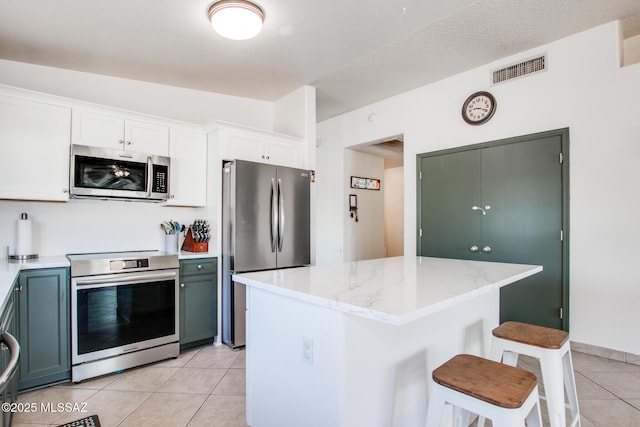 6075 N Applesauce Ct, Tucson, AZ 85741 - kitchen featuring appliances with stainless steel finishes, light tile patterned flooring, a breakfast bar area, a kitchen island, and light stone counters