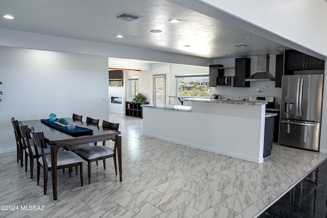 5051 N Hillcrest Dr, Tucson, AZ 85704 - kitchen with stainless steel refrigerator with ice dispenser, wall chimney range hood, recessed lighting, light stone counters, and dark cabinets