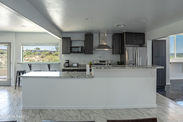 5051 N Hillcrest Dr, Tucson, AZ 85704 - kitchen with wall chimney range hood, appliances with stainless steel finishes, light marble finish flooring, a kitchen island with sink, and recessed lighting