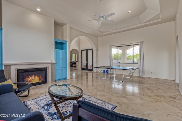 6859 N Placita Chula Vis, Tucson, AZ 85704 - living room featuring arched walkways, a tray ceiling, a glass covered fireplace, a ceiling fan, and a high ceiling
