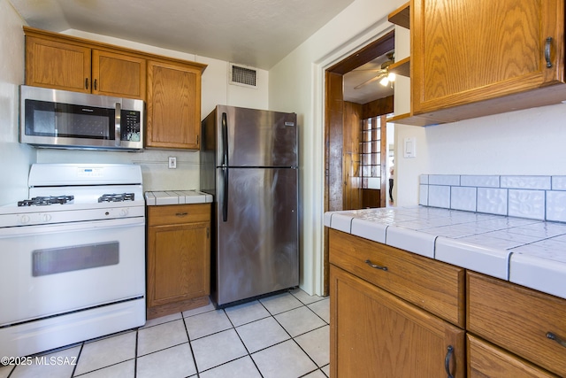 642 E 2nd St, Tucson, AZ 85705 - kitchen featuring appliances with stainless steel finishes, tile countertops, brown cabinets, a ceiling fan, and light tile patterned flooring