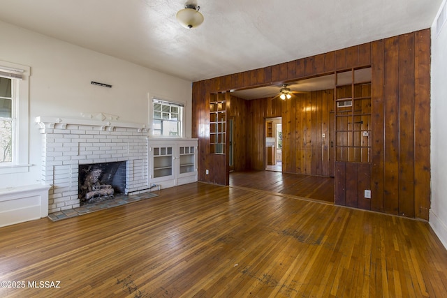 642 E 2nd St, Tucson, AZ 85705 - unfurnished living room featuring wooden walls, hardwood / wood-style floors, ceiling fan, and a brick fireplace