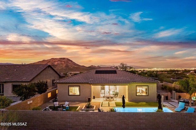 1144 S Castar Dr, Tucson, AZ 85745 - back of house at dusk with a tiled roof, a fenced backyard, roof mounted solar panels, a patio area, and stucco siding