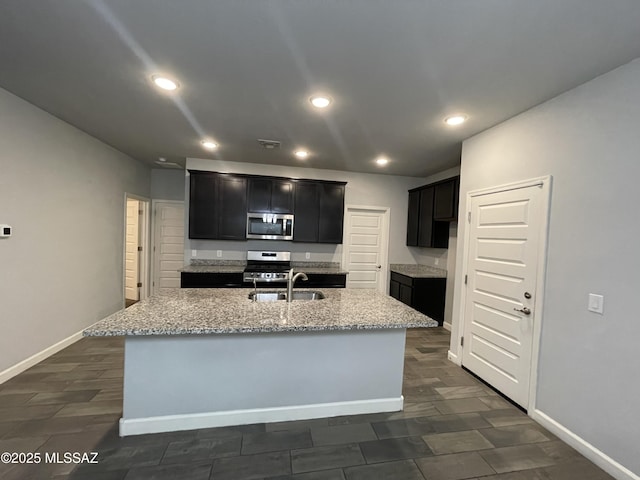 3306 N Baby Bruno Way, Tucson, AZ 85745 - kitchen featuring appliances with stainless steel finishes, an island with sink, light stone countertops, dark cabinets, and recessed lighting