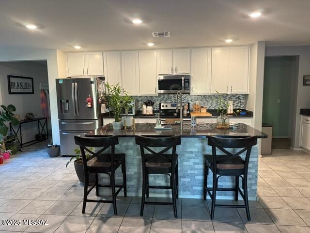 9150 N Wagon Spoke Ct, Tucson, AZ 85742 - kitchen featuring stainless steel appliances, decorative backsplash, light tile patterned floors, white cabinetry, and a breakfast bar