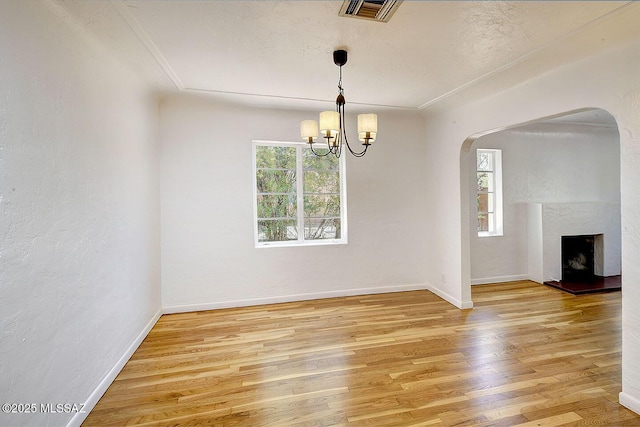2421 E Drachman St, Tucson, AZ 85719 - unfurnished room with arched walkways, light wood-style flooring, a chandelier, and a fireplace with raised hearth