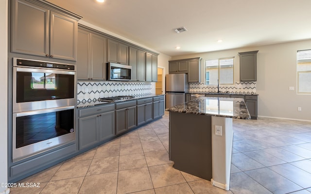 8820 E Stone Meadow Cir, Tucson, AZ 85730 - kitchen with appliances with stainless steel finishes, dark stone countertops, backsplash, a kitchen island, and light tile patterned floors