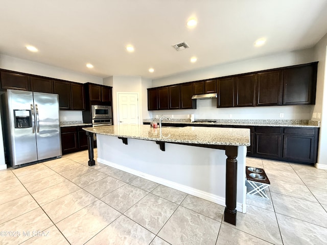 9636 N Havenwood Way, Marana, AZ 85653 - kitchen with stainless steel appliances, light stone counters, dark brown cabinets, under cabinet range hood, and light tile patterned flooring
