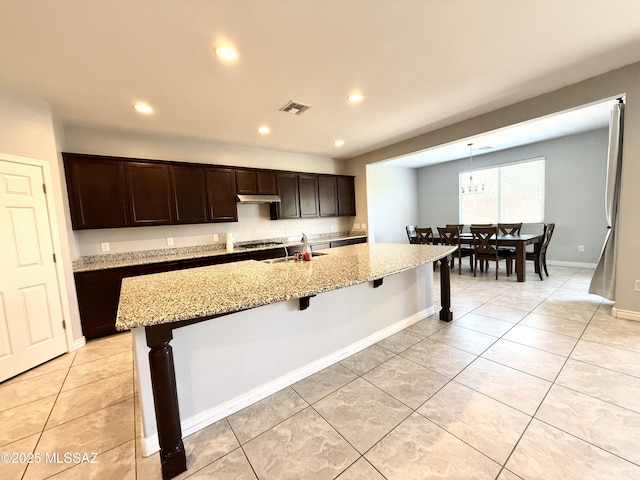 9636 N Havenwood Way, Marana, AZ 85653 - kitchen with light tile patterned flooring, dark brown cabinetry, a breakfast bar, recessed lighting, and under cabinet range hood