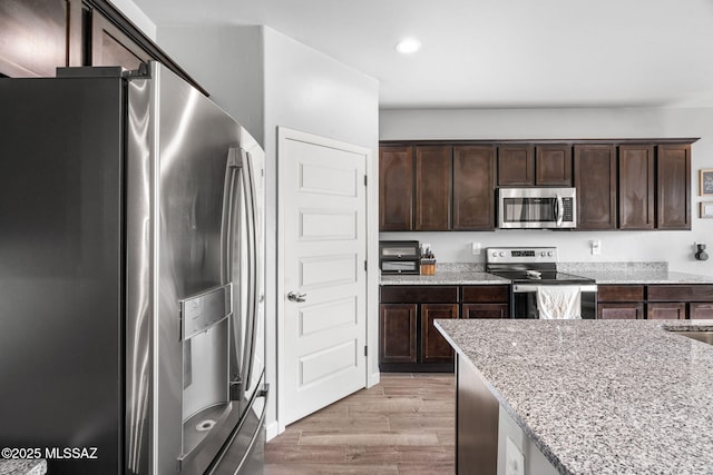 13331 N Carbine Ct, Marana, AZ 85653 - kitchen featuring stainless steel appliances, dark brown cabinetry, light stone countertops, light wood finished floors, and recessed lighting