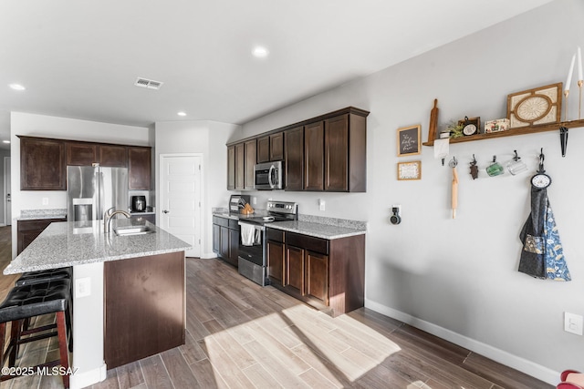 13331 N Carbine Ct, Marana, AZ 85653 - kitchen with stainless steel appliances, dark brown cabinets, light stone counters, a kitchen breakfast bar, and dark wood-style flooring
