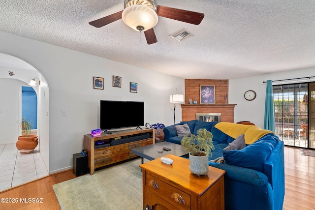 53 N Davila Cir, Tucson, AZ 85745 - living room featuring a textured ceiling, ceiling fan, light wood-style flooring, arched walkways, and a brick fireplace
