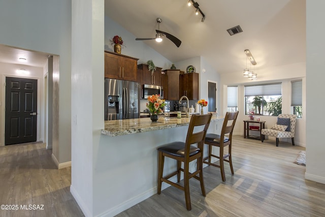 2856 W Goldfield Dr, Tucson, AZ 85745 - kitchen with appliances with stainless steel finishes, a ceiling fan, wood finished floors, a kitchen breakfast bar, and light stone countertops