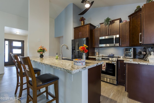 2856 W Goldfield Dr, Tucson, AZ 85745 - kitchen featuring stainless steel appliances, a kitchen bar, light wood-style flooring, dark brown cabinetry, and light stone countertops