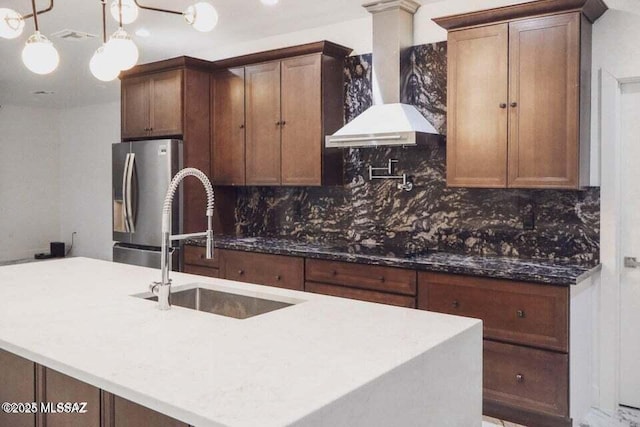 1886 Via Francia, Rio Rico, AZ 85648 - kitchen featuring wall chimney range hood, stainless steel fridge, tasteful backsplash, dark stone counters, and hanging light fixtures