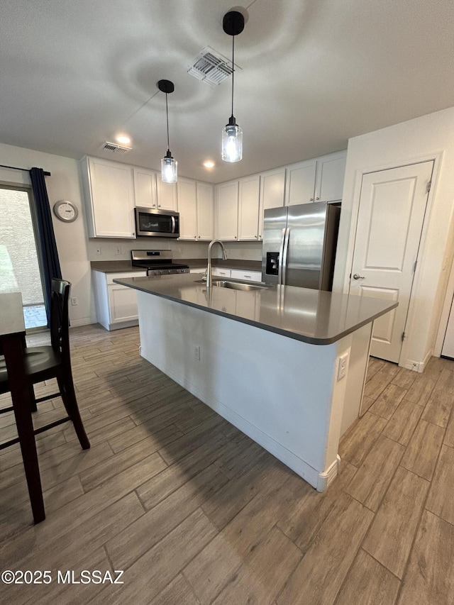 1126 E Descent St, Tucson, AZ 85719 - kitchen with appliances with stainless steel finishes, dark countertops, light wood-style flooring, white cabinets, and a kitchen island with sink